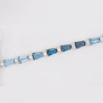 Macro close-up showing the four-prong settings holding the emerald-cut blue topaz stones and small accent diamonds securely in white gold.