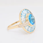 Gold ring with blue gemstone and diamond accents on a light gray background