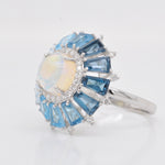 Macro shot detailing the prong-set cabochon opal, the fine Pave diamond halo, and the blue gemstone settings.