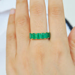A close-up of a model's hand wearing the 14K gold emerald ring on middle finger.