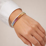 Rainbow gemstone and diamond bangle styled on a model’s wrist to show scale, fit, and elegant drape.