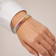 Rainbow gemstone and diamond bangle styled on a model’s wrist to show scale, fit, and elegant drape.