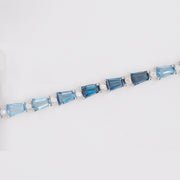 Macro close-up showing the four-prong settings holding the emerald-cut blue topaz stones and small accent diamonds securely in white gold.