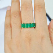A close-up of a model's hand wearing the 14K gold emerald ring on middle finger.