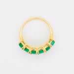 Dynamic angle focusing on the smooth gold shank and the sequence of green emeralds.