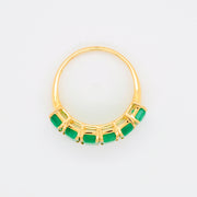 Dynamic angle focusing on the smooth gold shank and the sequence of green emeralds.