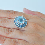 Close-up of a hand displaying the unique rotating blue gemstone ring against natural light.